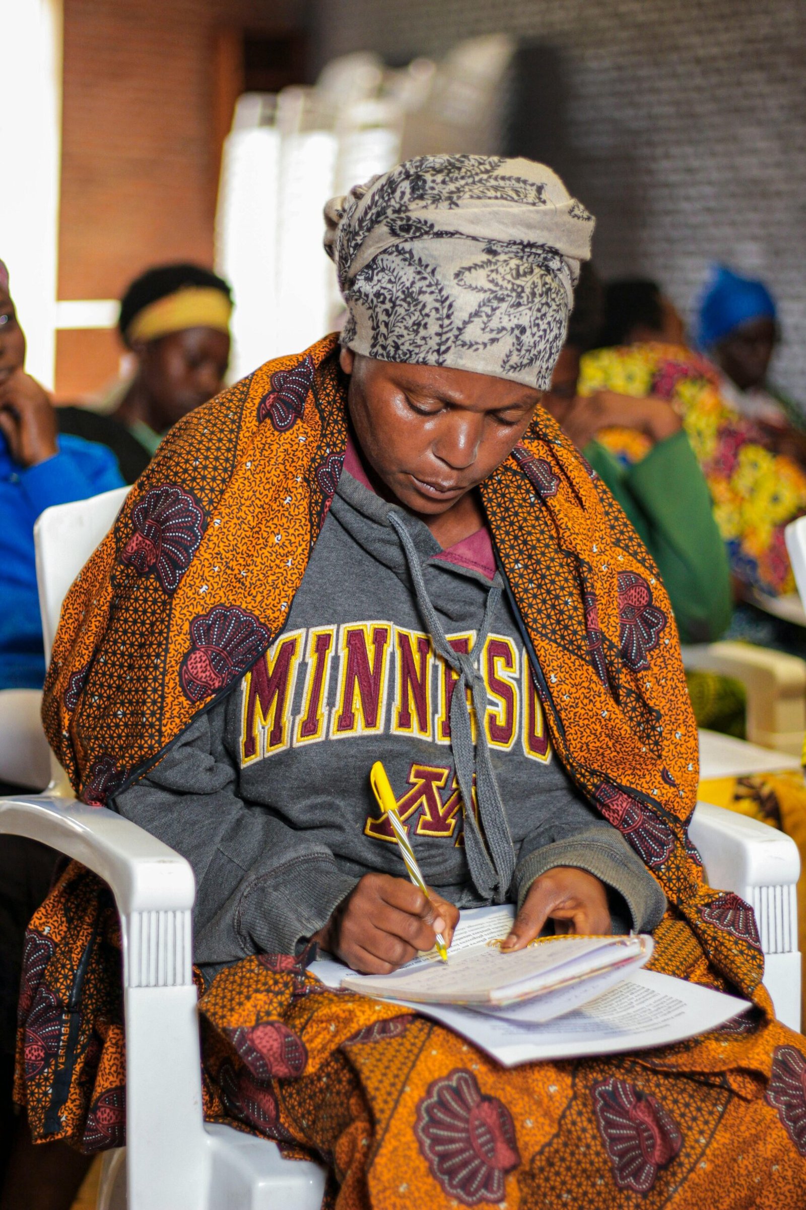 Woman in colorful African attire taking notes during a session in Gitega, Burundi.